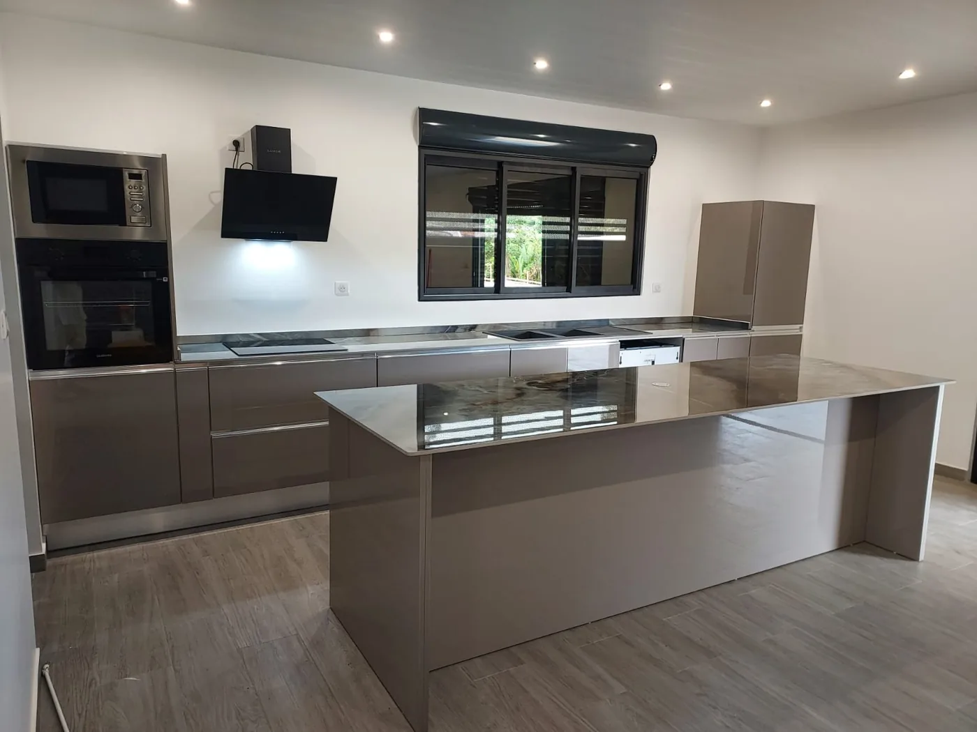 Cuisine taupe brillante avec îlot central et hotte suspendue